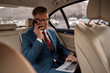 © Svitlana - Making money. Confident and stylish mature businessman in full suit working on his laptop and talking on the phone with business partner while sitting in the car