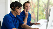 Business Background Of Asian And Caucasian Male Customer Service Agents On Telephone Service To Customers At Helpdesk Call Center And Customer Service Operation Center