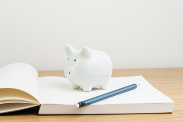 Canvas Print - Income, tax, savings, personal finance planning or investment concept, white piggy bank on blank opening note book with pencil on wooden table