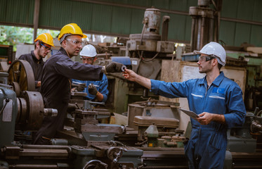 The Industry engineering and teamwork wearing safety uniform control operating lathe grinding machine working in industry factory.