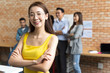 © saksit - Portrait of young Asian business woman at at creative office workplace. team in meeting in background