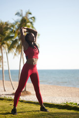 Wall Mural - Beautiful young Black woman stretching back after running on the beach in the morning