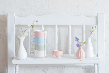 cups and vases with spring flowers on vintage wooden white shelf