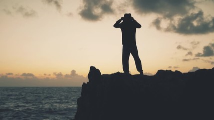 Wall Mural - A man in a jacket stands on a rock by the sea in a stormy weather at dawn	