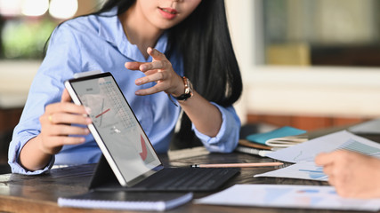 Leinwandbilder - Woman working as Business development showing/talking about information graphs in computer tablet while sitting at the modern meeting table with orderly office as background.