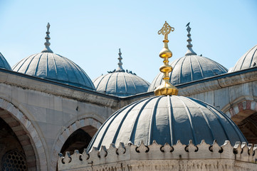 Dramatic sunlit view of the weathered domes with a golden spire on the gazebo of the Blue Mosque under bright blue sky in Istanbul, Turkey