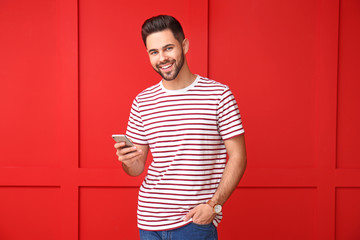 Wall Mural - Handsome young man with mobile phone on color background