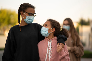 three young teens or preteens walking  on a street wearing street clothes and  surgical face mask to protect against an epidemic of diseases or viruses