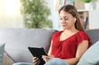 © Antonioguillem - Woman playing videos in a tablet sitting on a couch