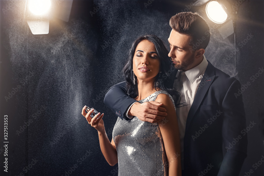 Stylish young couple with perfume on dark background