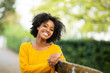 © mimagephotos - Close up of happy young black woman relaxing on bench outdoors