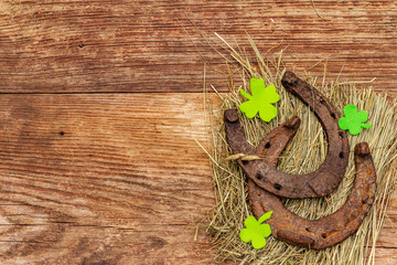 Two cast iron metal horse horseshoes with felt clove leaves on hay. Good luck symbol, St.Patrick's Day concept