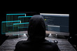 © LIGHTFIELD STUDIOS - back view of hooded hacker sitting near computer monitors with data on screens on black