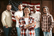 A Team Of American Patriots Against The Background Of A Wooden Wall With An American Flag. A Multi-National Group Of Young Businessmen Smiles At The Camera. Successful Start Up Concept.