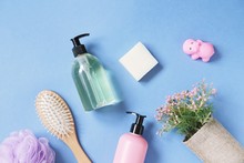 Purple Sponge, Wooden Hair Brush, Face Wash Gel, Natural Soap, Shower Gel, Flowers And Toy Hippo On A Blue Background. Flat Lay Beauty Photography. Toiletries Essentials