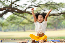 Happy African American Little Girl Smiling And Raises Her Hand While Sitting In The Park