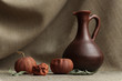 Still life of dried tangerines and leaves with a clay brown jug on a natural material
