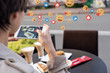 © insta_photos - Female blogger influencer hold phone take food mobile photo on phone sit at cafe table. Girl vlogger shoot social media instagram post on smartphone get many likes emoji over shoulder closeup view.