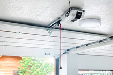 Opening Door And Automatic Garage Door Opener Electric Engine Gear Mounted On Ceiling With Emergency Cord. Double Place Empty Garage Interior With Rolling Entrance Gate