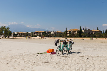 PARALIA, GREECE - SEPTEMBER 10, 2018: Beach scene. Two bicycles parked on the sandy beach and hotels at the background