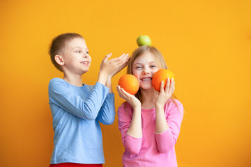 cute kids on an orange background with fruit play, put on their heads and laugh