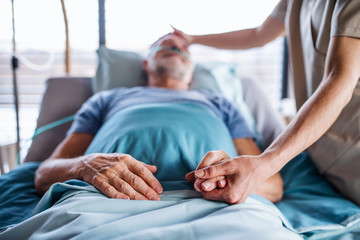 Wall Mural - Unrecognizable female doctor examining senior man in bed in hospital.