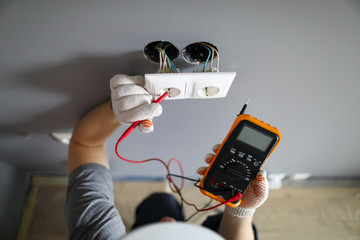 Man in hard hat and protective gloves checking wal outlet with tester