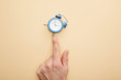 © LIGHTFIELD STUDIOS - cropped view of man touching small alarm clock on beige background