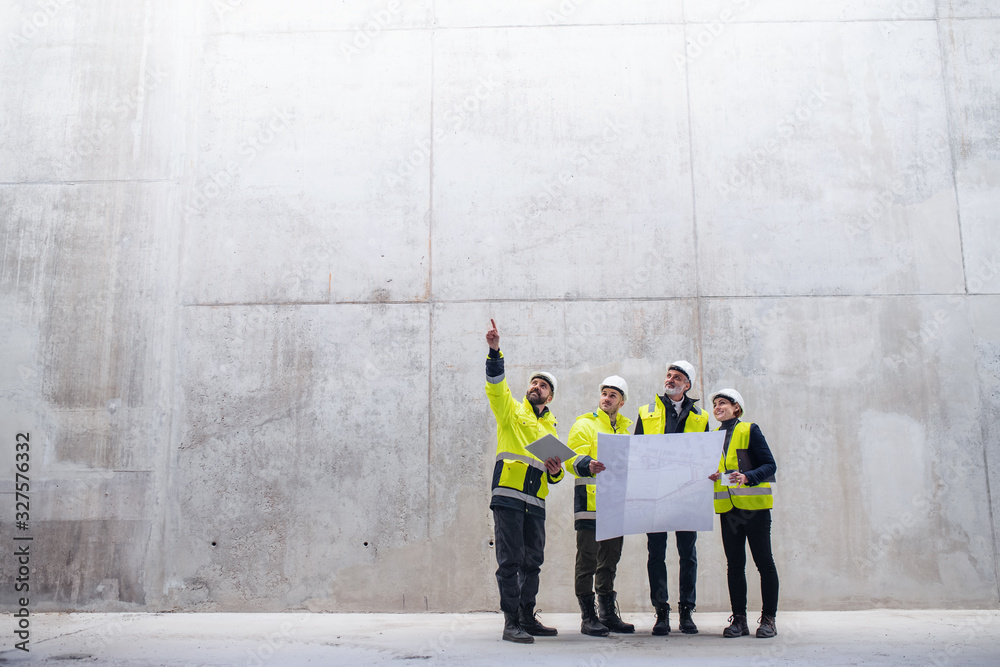 A group of engineers standing against concrete wall on construction site. - obrazy, fototapety, plakaty 