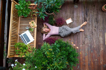 Wall Mural - Top view of senior woman with laptop lying outdoors on terrace, resting.