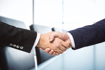 Two businessmen shake hands on the background of sunny meeting room, deal concept, close up