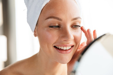 Canvas Print - Photo of young joyful woman doing makeup while looking in mirror