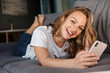 © Drobot Dean - Image of happy woman smiling and using cellphone while lying on sofa