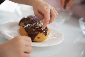 Child decorating a delicious home made chocolate covered doughnut with sprinkles