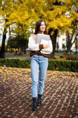 Young beautiful woman student walking in the park holding laptop computer.