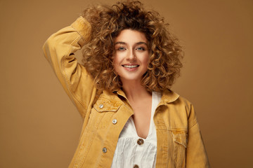 Happy young woman with curls posing at studio on brown studio background. Blonde woman with afro hairstyle smiling