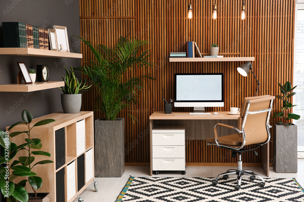 Comfortable workplace with computer near wooden wall in stylish room interior. Home office design - obrazy, fototapety, plakaty 