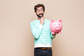 Wall Mural - young cool man holding a piggy bank against clean wall