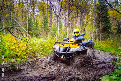 ATV. Man on a quad bike in the mud. The ATV overcomes dirt on the road. Yellow ATV in the forest. Concept - extreme sports. A man overcomes the terrain. Concept - quad bike store. Biker