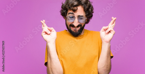 young crazy cool man smiling and anxiously crossing both fingers, feeling worrie Poster Mural XXL