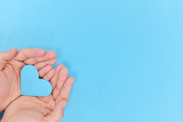 blue heart shape cutout on hands in blue background. top view, kindness and charity concept.