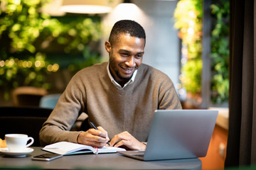 Wall Mural - Black business guy taking notes in notebook holding tablet