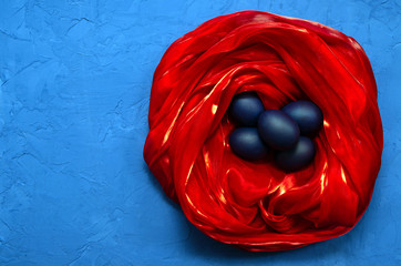 blue trendy modern eggs in a red silk nest on a classic blue background with place for text