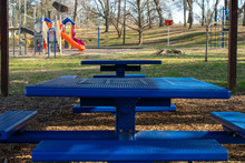 Blue Metal Benches In A Park In The Shade With A Playground In The Background