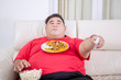 Fat man grabbing popcorns while holding tv remote