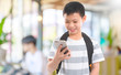 © bunditinay - Happy Asian boy backpack is using smartphone isolated on blur classroom school interior background with Smiling face.Concept of people using technology.