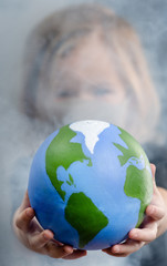 Wall Mural - Little girl holds planet in the smoke. Global warming. The concept of disaster