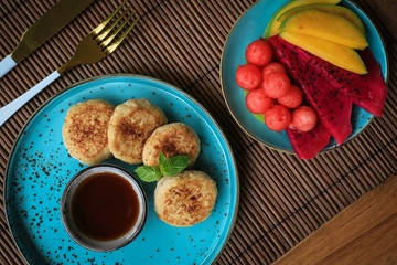 Wall Mural - Vegan tofu cheese pancakes on blue plate with fresh tropical fruits and coconut cream, top view