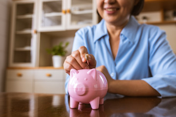 Wall Mural - Asain Elder  putting coin money to piggy bank saving, family, savings, age and people concept - smiling senior couple with money and piggy bank at home.