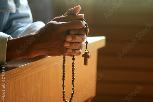 Cuadros en Lienzo Senior man kneel, holding wooden rosary beads in hand with Jesus Christ holy cross crucifix in the church